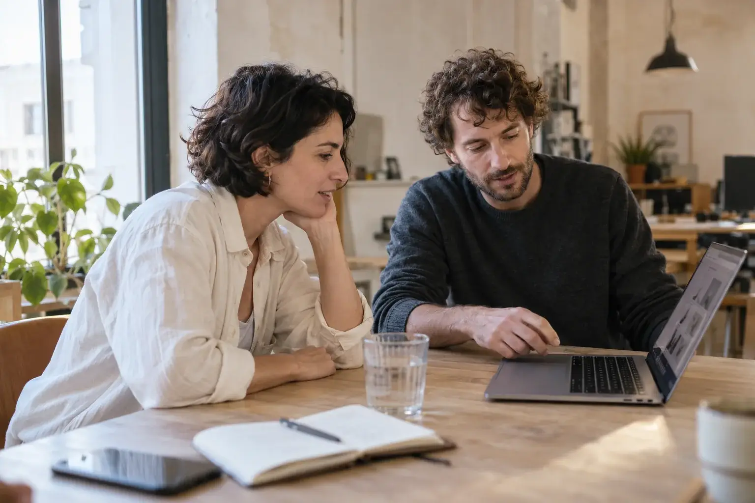 Dos personas conversan sobre un proyecto web junto a un portátil